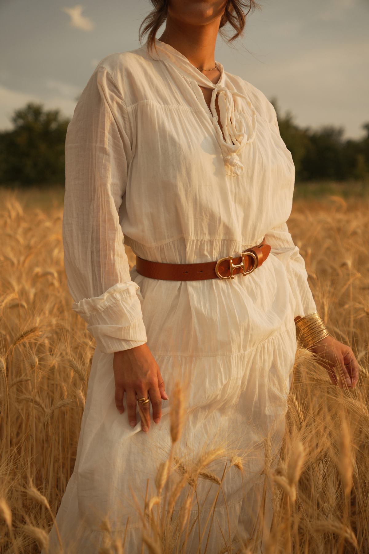 Ceinture femme en cuir camel Jeanne Atelier Nappa, boucle mors dorée sur une robe blanche, avec bijoux dorés