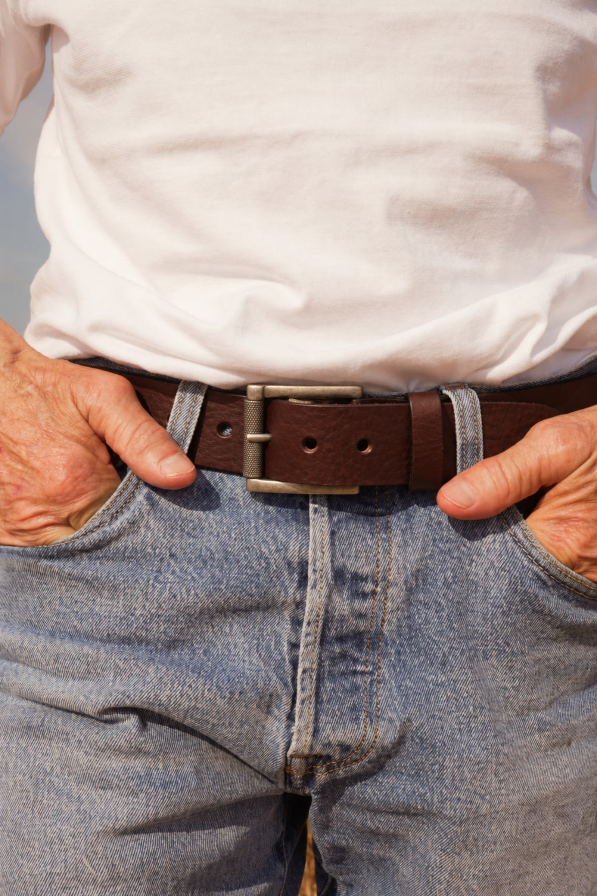 Ceinture homme Max Atelier Nappa en cuir marron foncé à boucle à rouleau, portée sur un jean délavé avec un t-shirt blanc