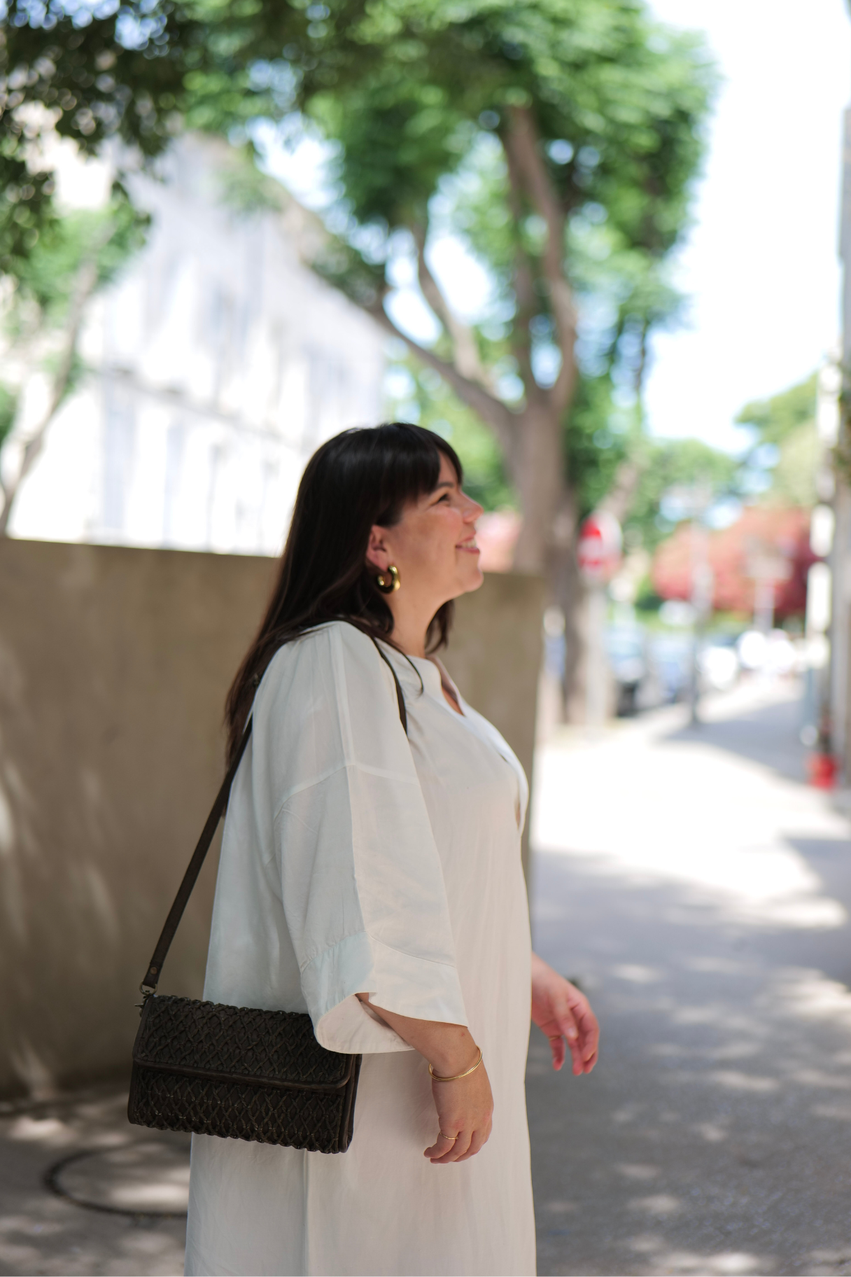 Pochette en cuir tressé kaki portée en bandoulière par une femme en robe blanche, look estival urbain