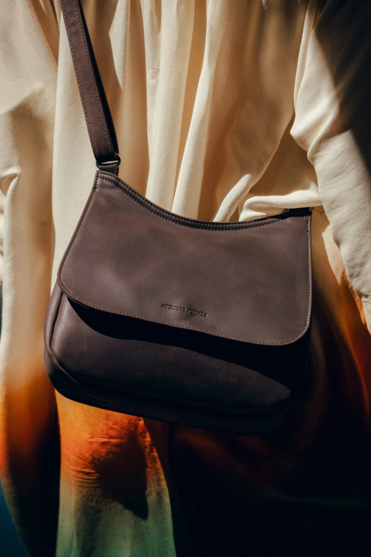 Sac Artémis Compact en cuir chocolat porté en bandoulière, logo embossé sur le rabat