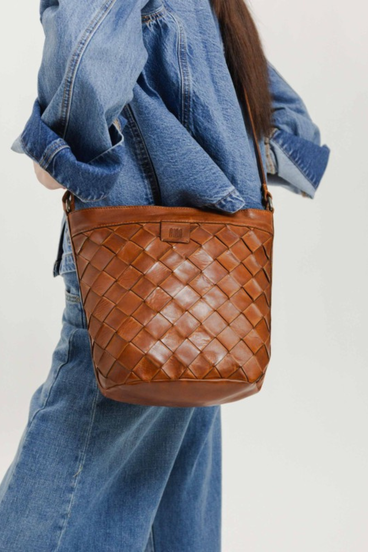 Sac seau en cuir tressé main coloris cognac porté à l'épaule, maroquinerie Nappa