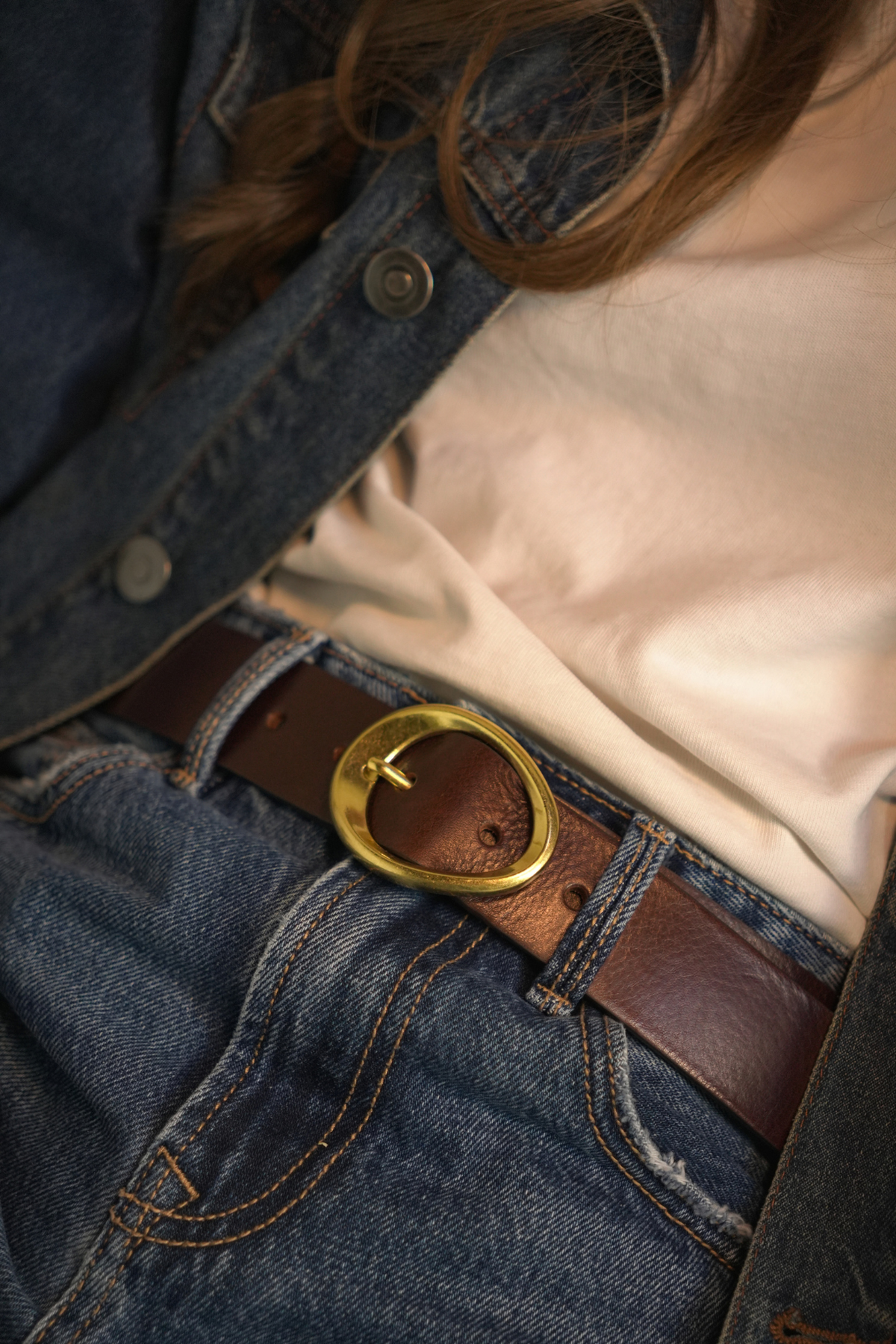 Ceinture Celya Atelier Nappa à boucle organique dorée sur un jean brut, avec un t-shirt écru et une veste en jean