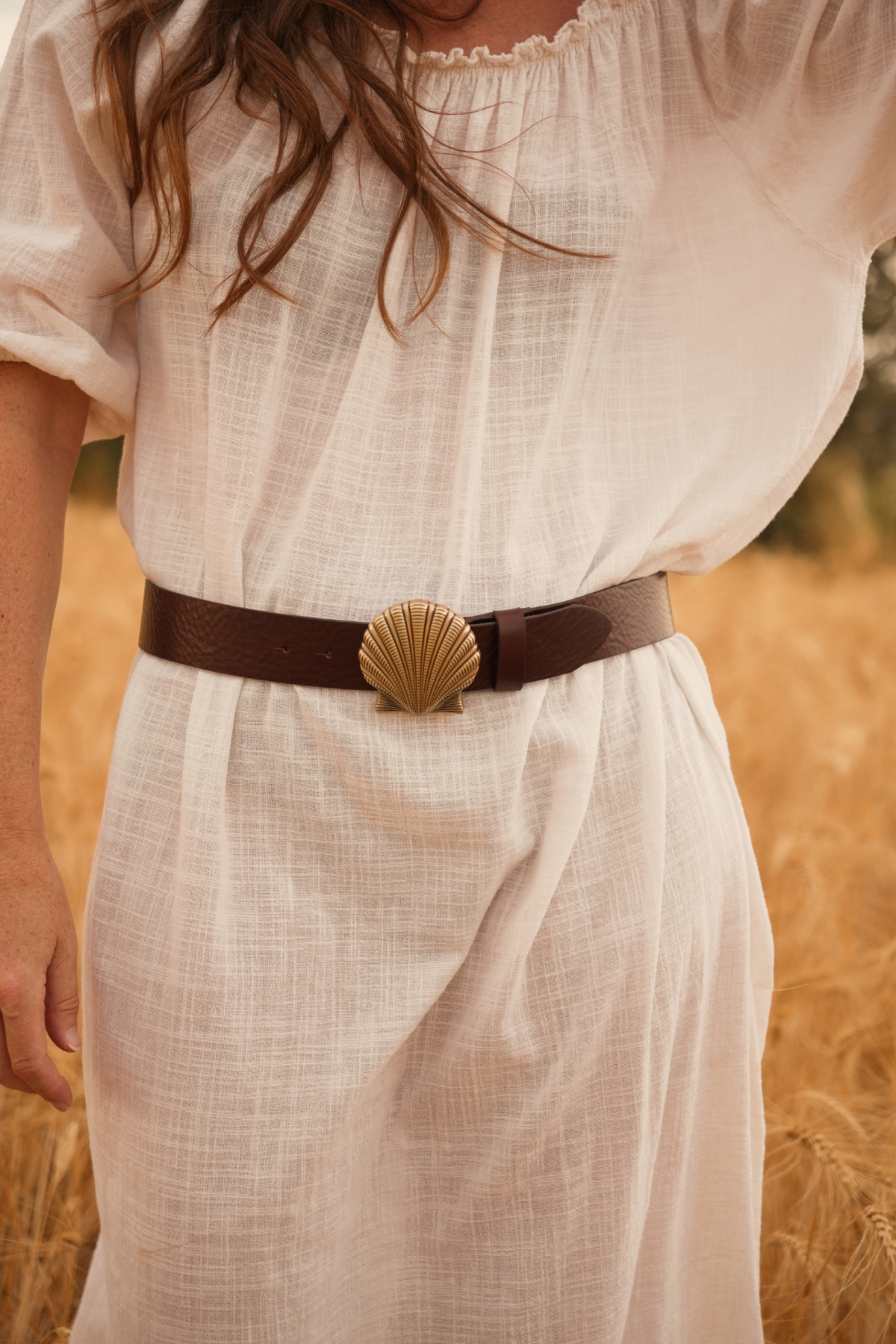 Ceinture en cuir marron foncé Juliette Atelier Nappa, boucle coquillage dorée sur une robe en lin blanc.