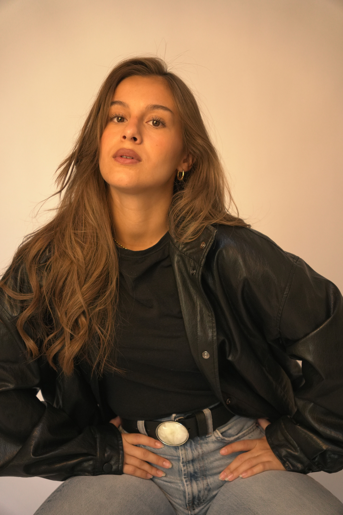 Ceinture Manar Atelier Nappa en cuir noir à boucle plaque ovale blanche, portée avec un jean et une veste en cuir