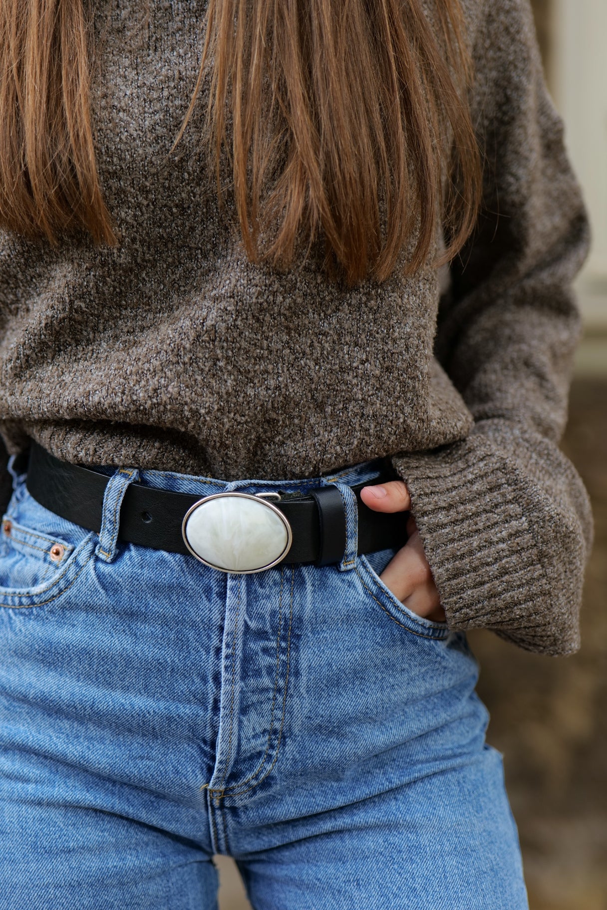 Gros plan sur la boucle plaque ovale blanche de la ceinture Suzanne en cuir noir