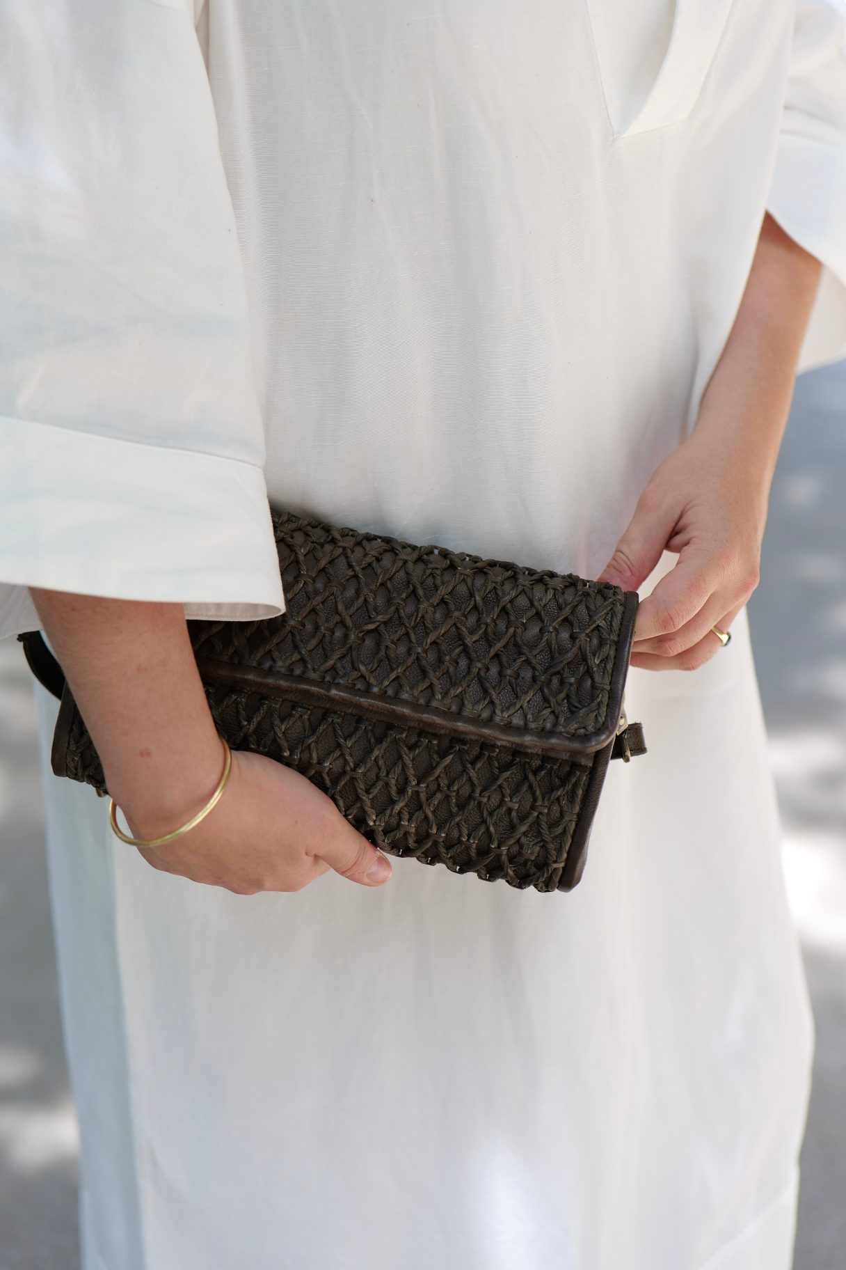 Pochette en cuir tressé vert kaki tenue à la main avec robe blanche fluide, look élégant