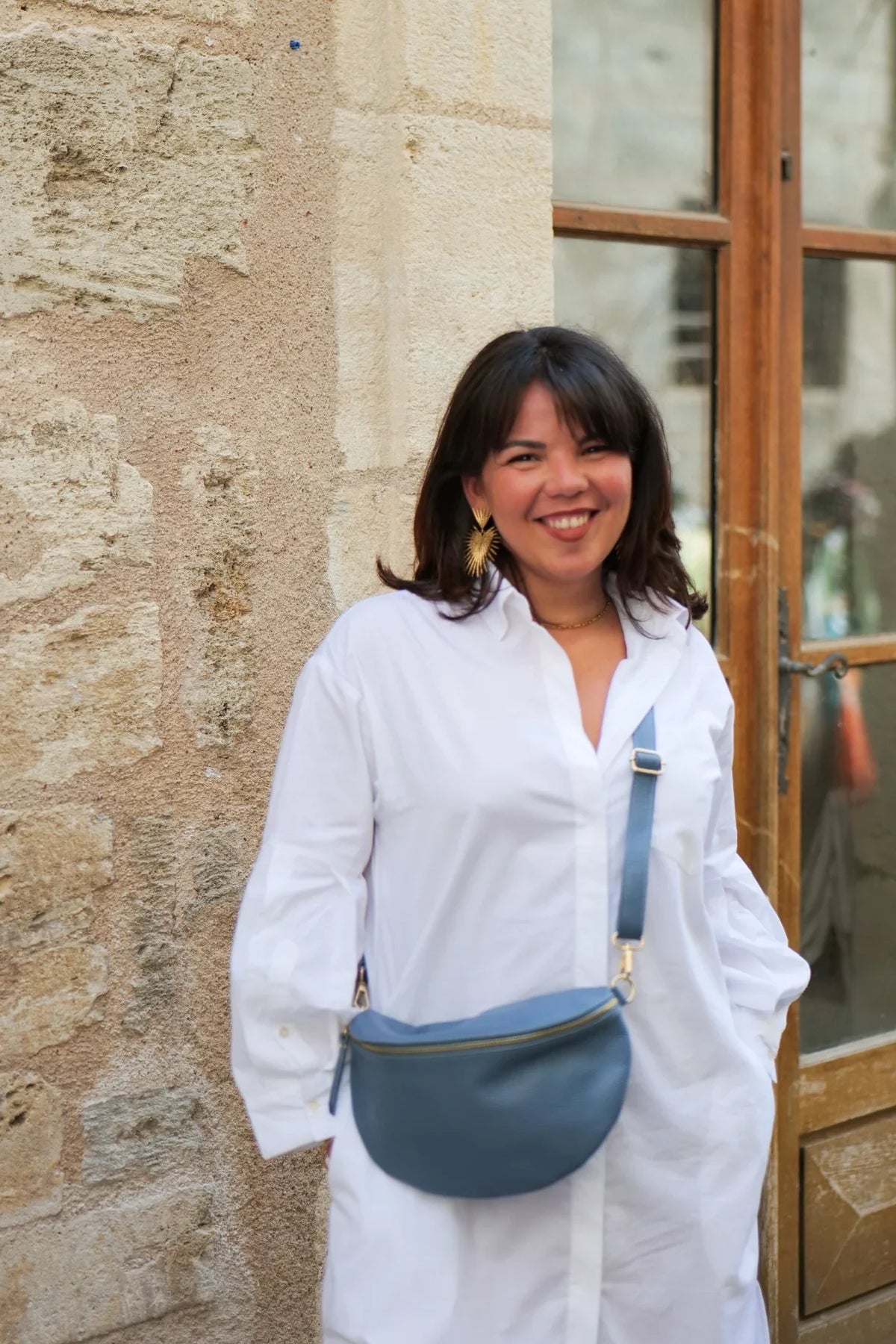 Sac banane Jeanne en cuir grainé bleu clair porté en travers sur une chemise blanche