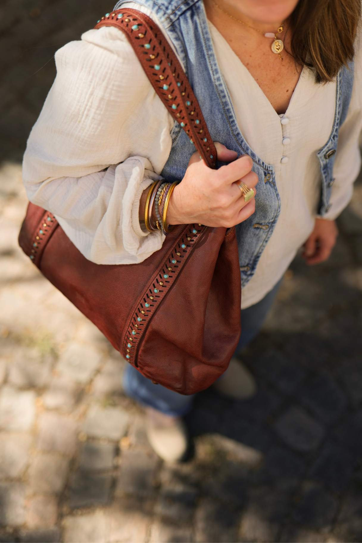 Gros plan sur sac en cuir marron cognac avec détails perlés turquoise et clous dorés, finitions bohèmes