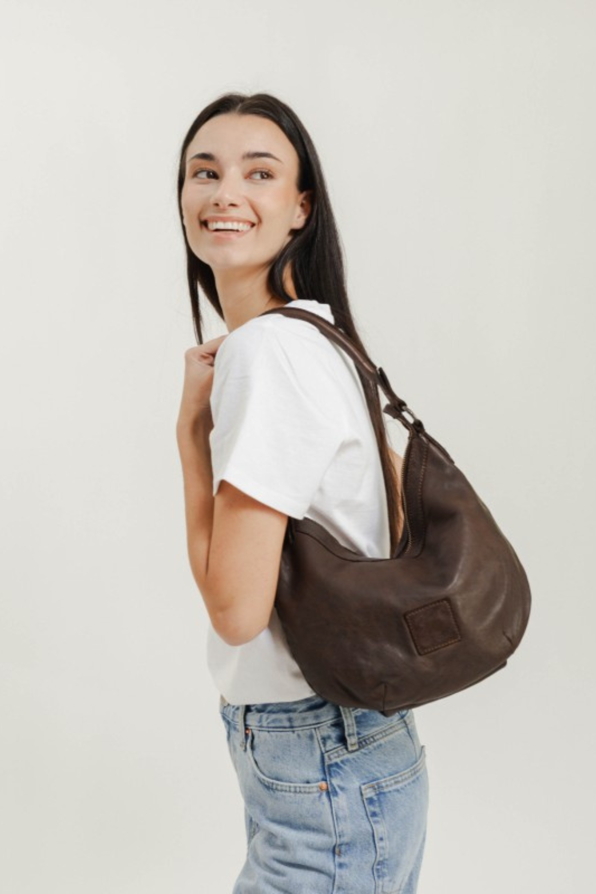 Sac hobo en cuir marron foncé porté à l'épaule avec un t-shirt blanc et un jean